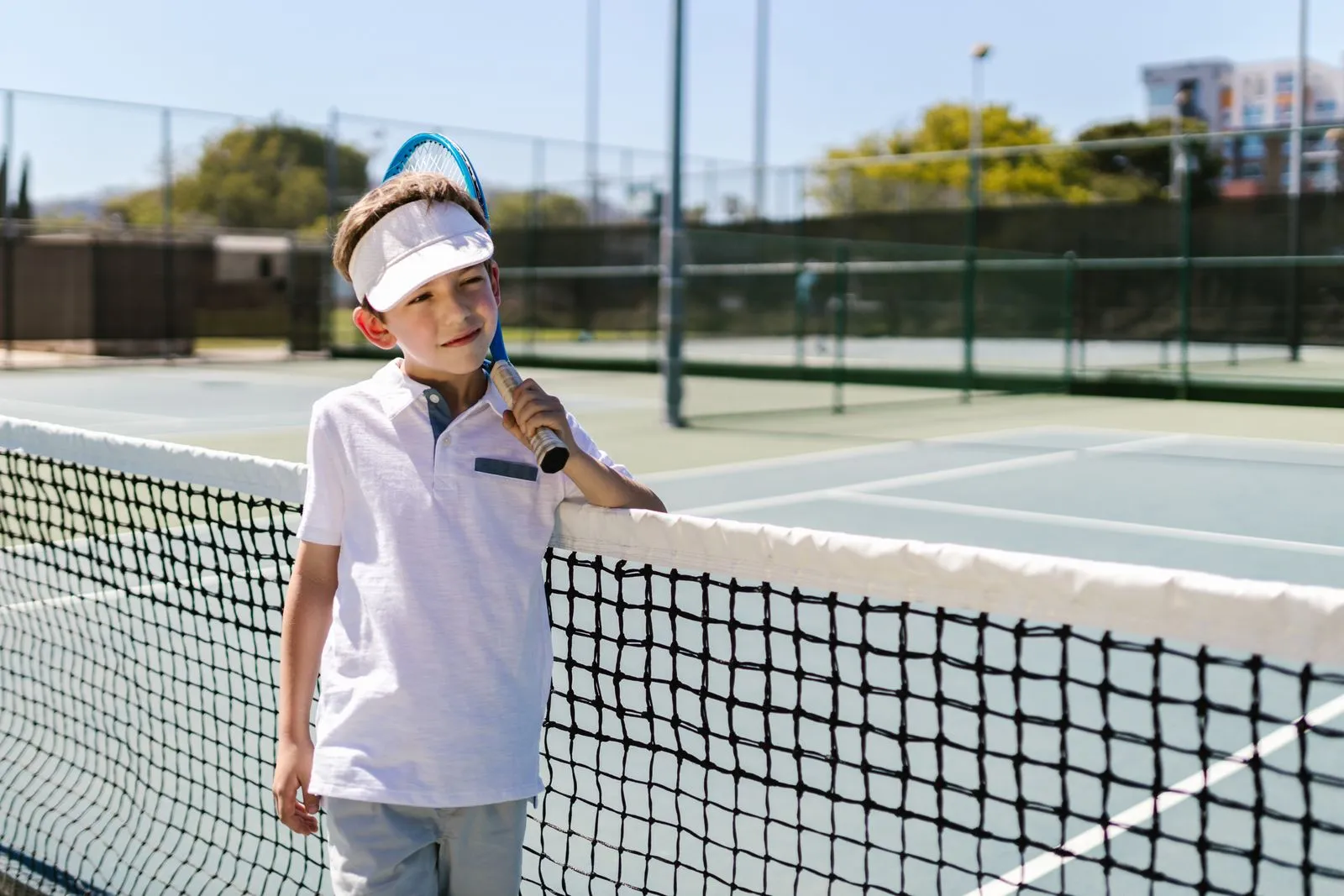 Child in tennis attire posing with a racket on an outdoor court.